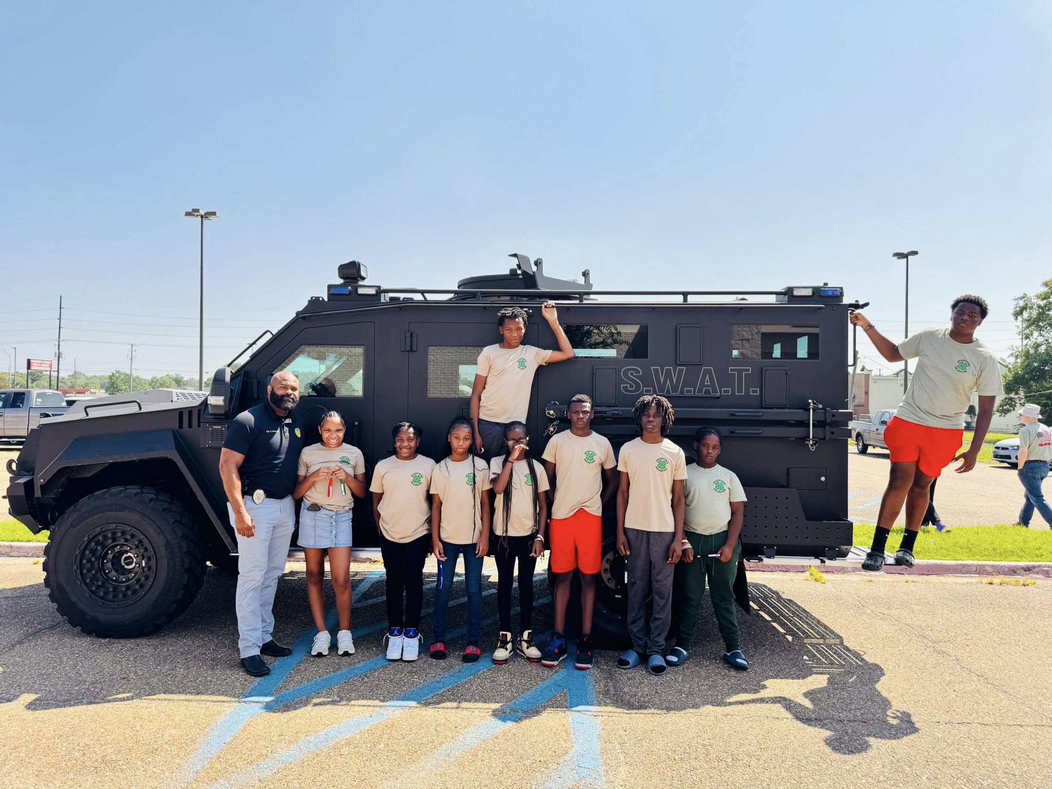 A police officer and some kids posing by a S.W.A.T. vehicle.